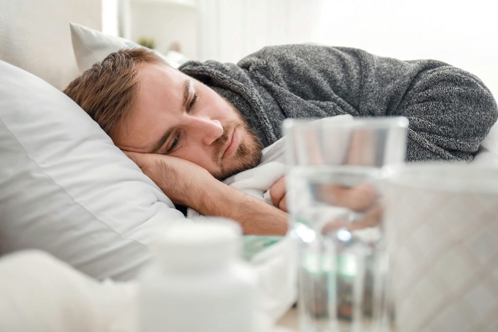 Man laying in bed with water and medication on the bedside table.