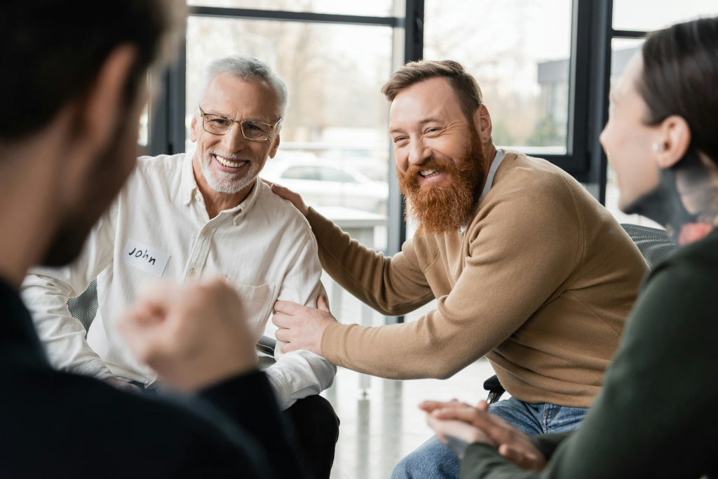 Man braces shoulder of father sitting next to him in gambling support meeting.