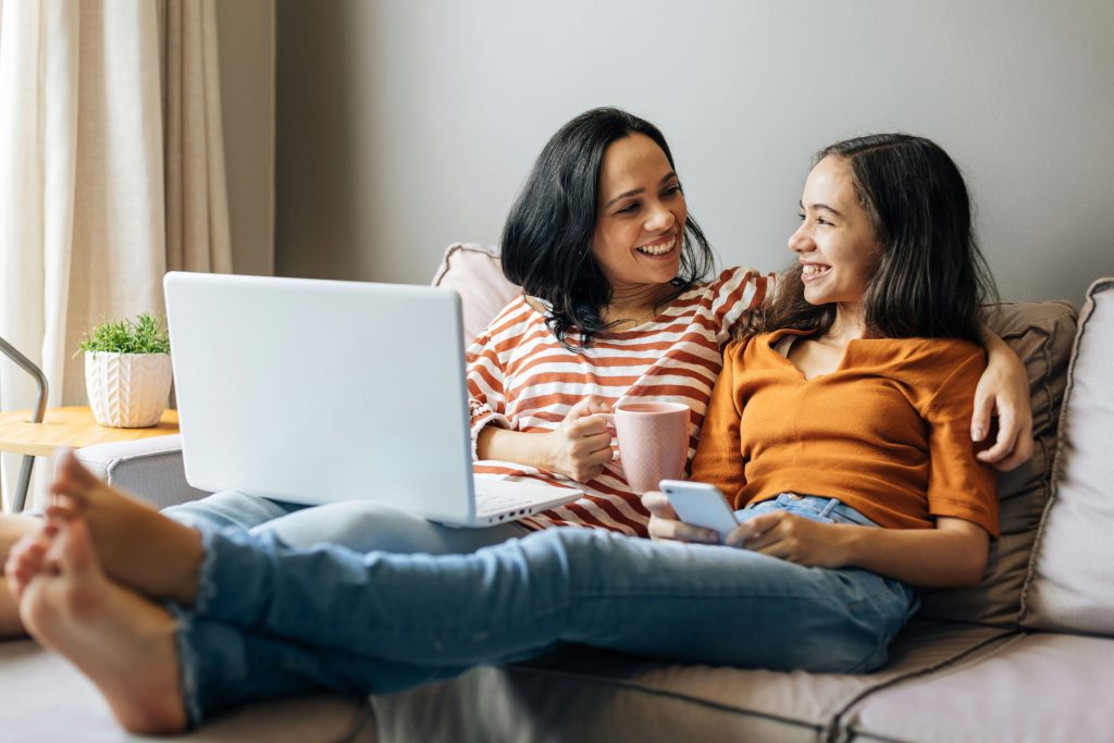 Mother and daughter drinking coffee while reading articles on a laptop.